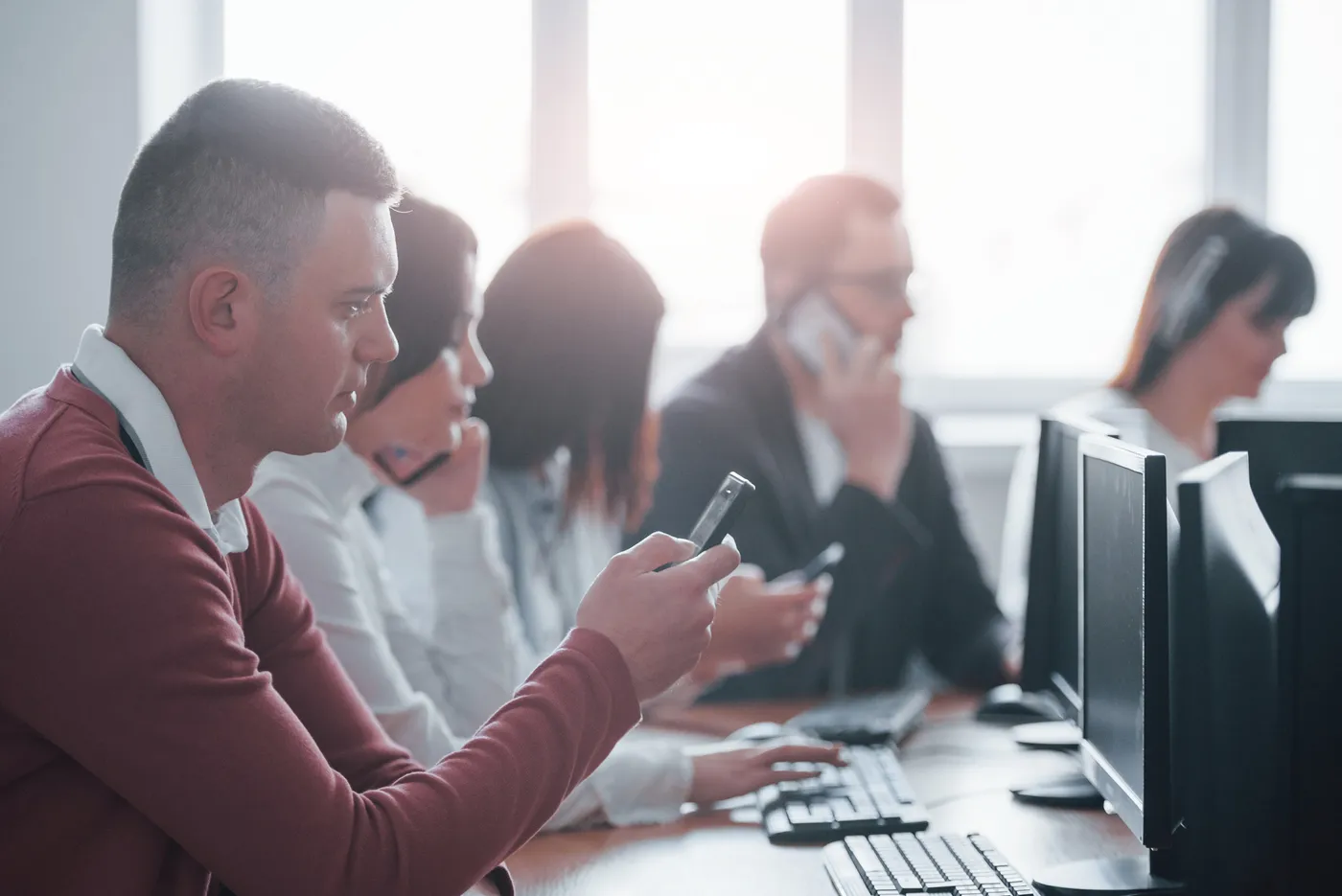 Des professionnels en bureau échangent par téléphone et travaillent sur leurs ordinateurs.