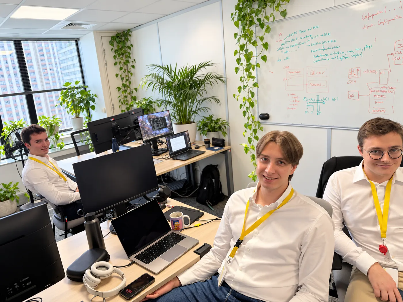 Trois membres souriants de l’équipe Stelau à leurs postes de travail, dans un bureau lumineux agrémenté de plantes.
