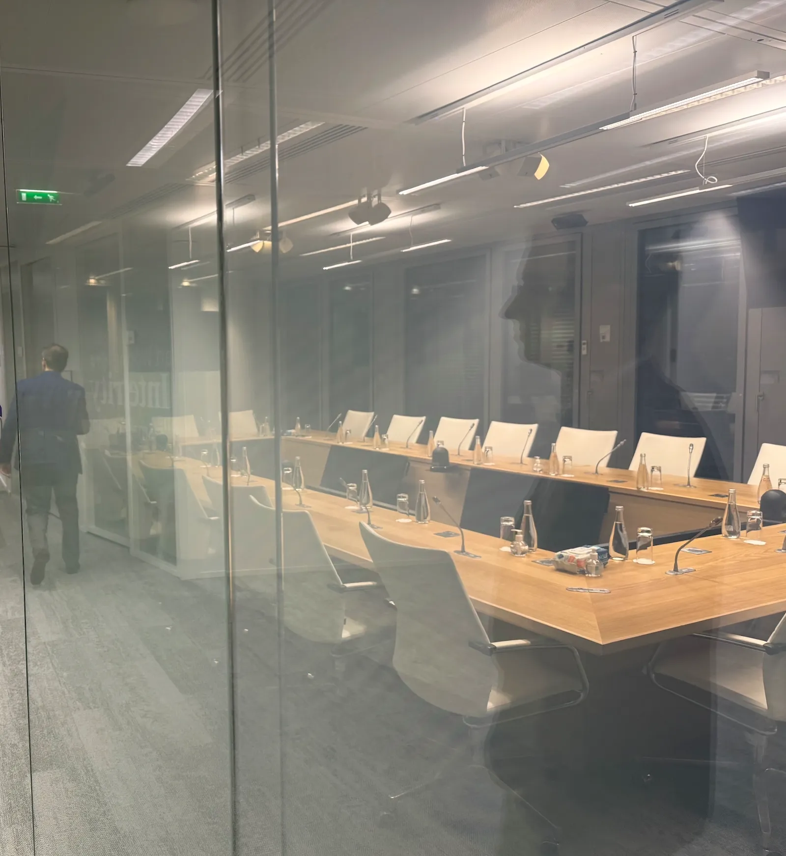 A meeting room equipped with microphones, seen through a glass partition.
